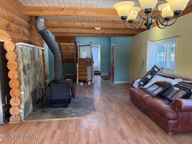 unfurnished living room with wooden ceiling, wood finished floors, beam ceiling, a wood stove, and an inviting chandelier