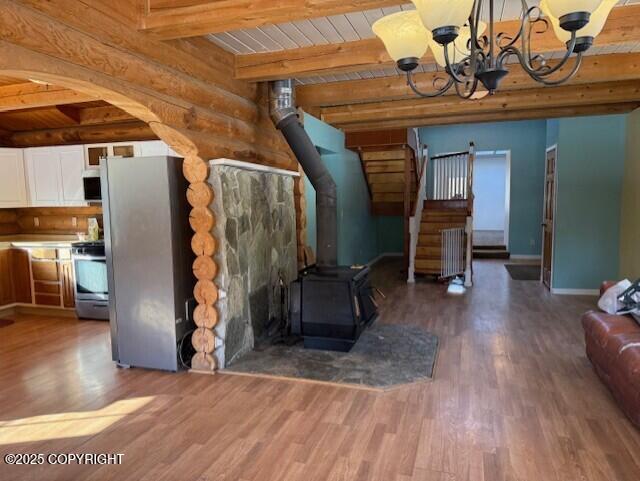 unfurnished living room featuring beam ceiling, rustic walls, a wood stove, wood finished floors, and stairs