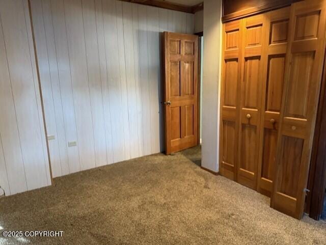 unfurnished bedroom with wood walls, a closet, and carpet flooring