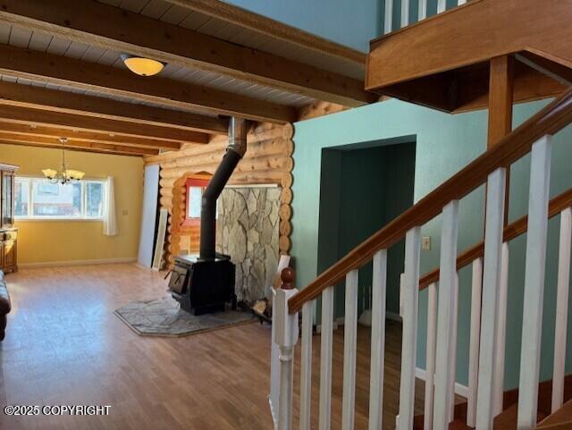 unfurnished living room with log walls, a wood stove, wood finished floors, beamed ceiling, and stairs