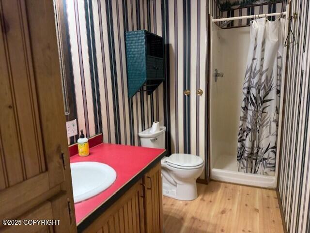 bathroom with toilet, wood finished floors, vanity, a shower stall, and wallpapered walls