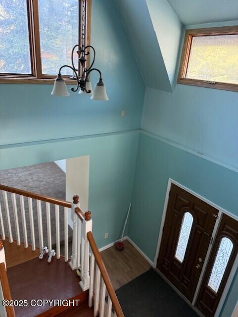 foyer entrance featuring a chandelier, wood finished floors, baseboards, vaulted ceiling, and stairs