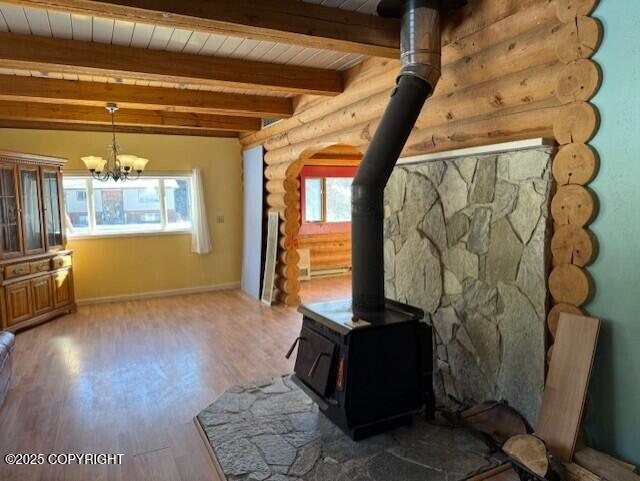 unfurnished living room featuring a notable chandelier, wood finished floors, wood ceiling, beam ceiling, and a wood stove