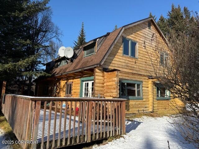 snow covered rear of property with a wooden deck and a gambrel roof