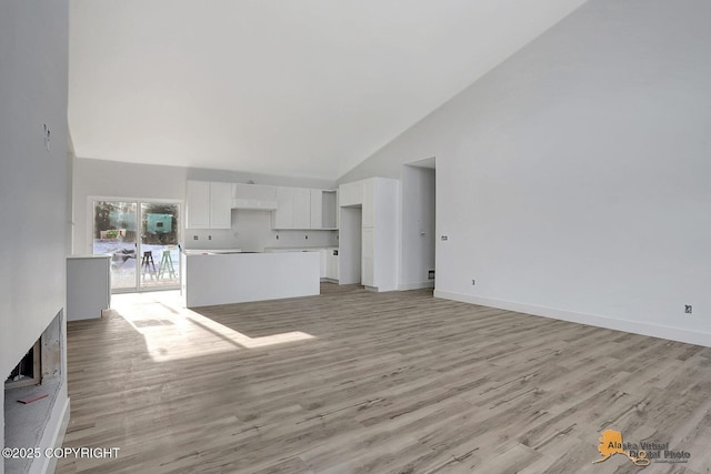 unfurnished living room with high vaulted ceiling, light wood-style floors, and baseboards