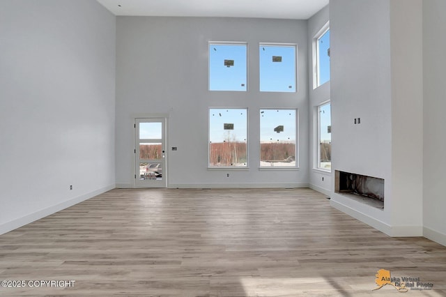 unfurnished living room with a high ceiling, light wood-style flooring, a fireplace, and baseboards