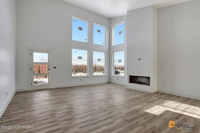 unfurnished living room featuring a high ceiling, a fireplace, wood finished floors, and baseboards