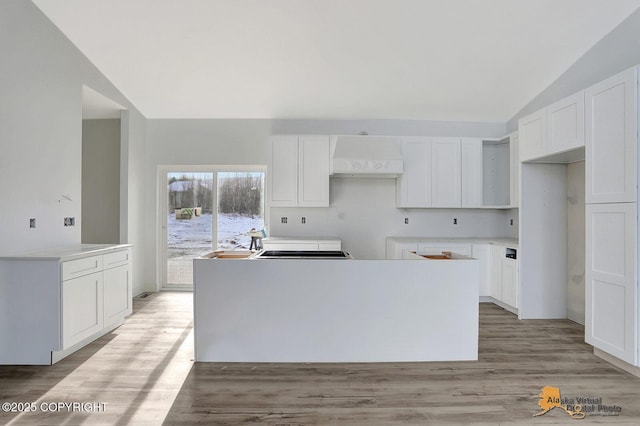 kitchen featuring a center island, white cabinets, vaulted ceiling, light wood-type flooring, and extractor fan