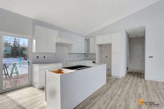 kitchen featuring lofted ceiling, a kitchen island, white cabinetry, and custom range hood