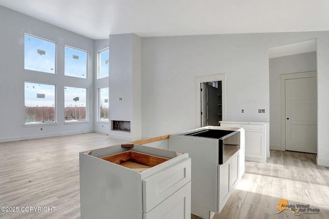 kitchen with a towering ceiling, light wood-style flooring, baseboards, and white cabinets