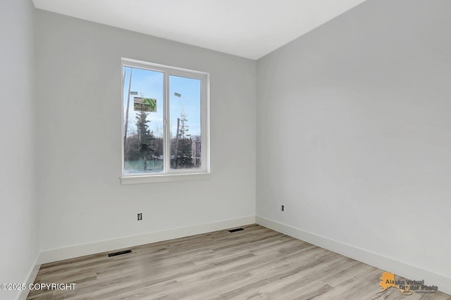 empty room with light wood finished floors, visible vents, and baseboards