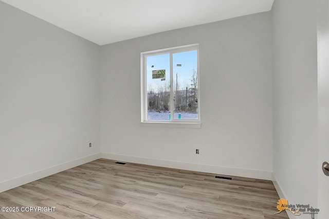 unfurnished room with light wood finished floors, visible vents, and baseboards