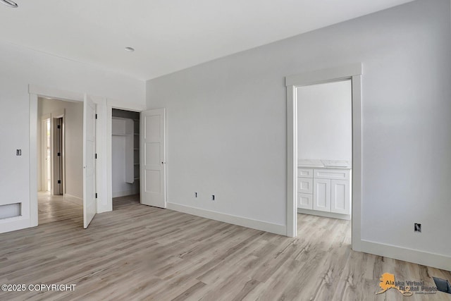 unfurnished bedroom featuring a closet, connected bathroom, light wood-style flooring, and baseboards