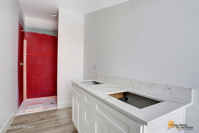 kitchen featuring light stone counters, a sink, baseboards, white cabinets, and light wood finished floors