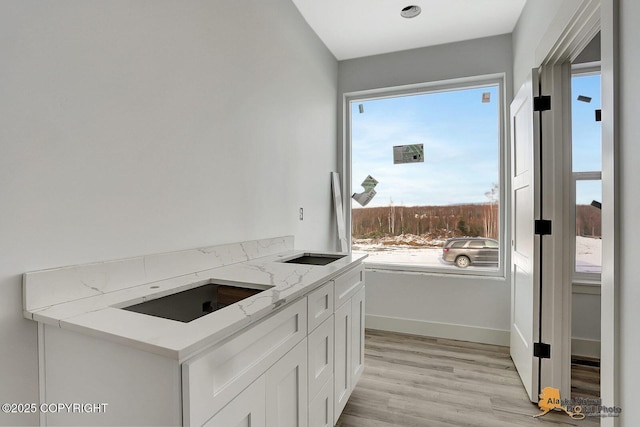 kitchen featuring light stone counters, white cabinetry, light wood-style floors, and baseboards