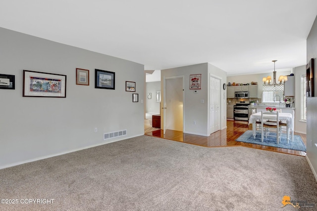 unfurnished living room with carpet floors, an inviting chandelier, baseboards, and visible vents