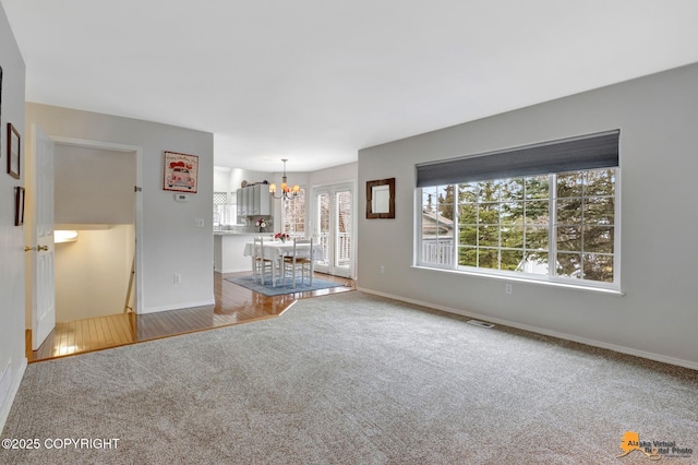 unfurnished living room featuring carpet floors, baseboards, visible vents, and a chandelier