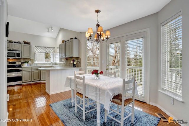 dining room featuring light wood-style floors, baseboards, vaulted ceiling, and an inviting chandelier