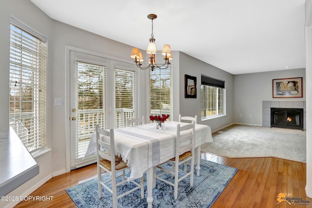 dining area with a tile fireplace, light wood-style flooring, baseboards, and an inviting chandelier