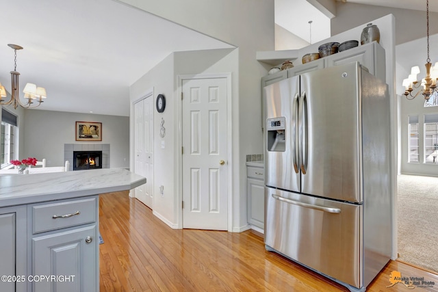 kitchen featuring a chandelier, a fireplace, stainless steel refrigerator with ice dispenser, and light wood-style flooring