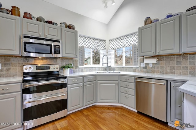 kitchen with vaulted ceiling, gray cabinets, stainless steel appliances, light wood-style floors, and a sink