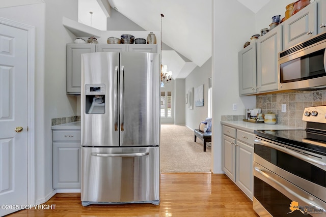 kitchen featuring stainless steel appliances, light countertops, light wood-style flooring, decorative backsplash, and vaulted ceiling