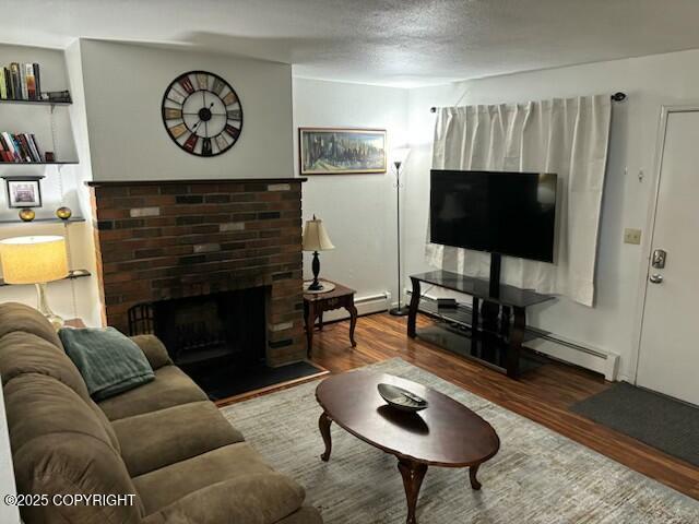 living room featuring a textured ceiling, a fireplace, a baseboard heating unit, and wood finished floors