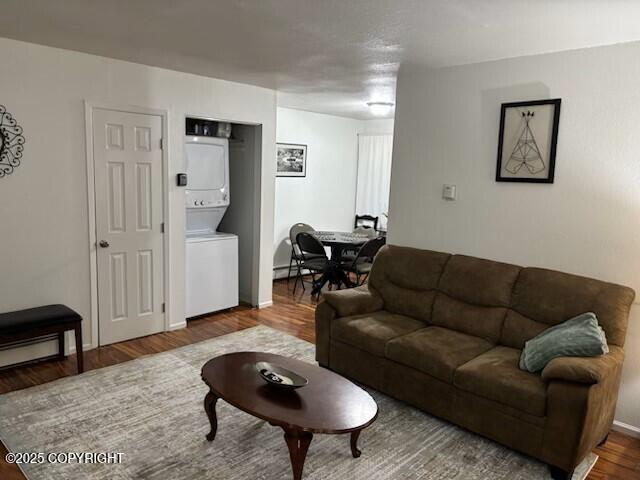 living area with a baseboard radiator, wood finished floors, and stacked washer / drying machine