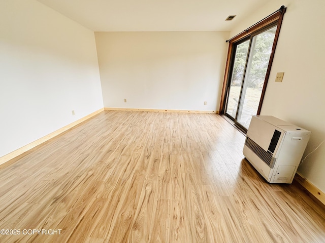 spare room with baseboards, heating unit, visible vents, and light wood-style floors