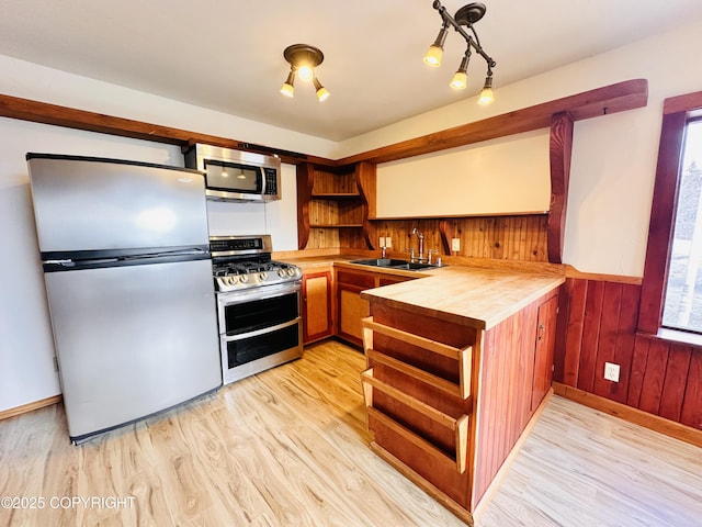 kitchen featuring stainless steel appliances, wood walls, a sink, light wood-type flooring, and open shelves