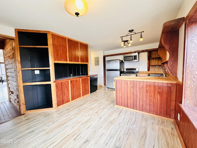 kitchen with appliances with stainless steel finishes, light wood-style floors, brown cabinetry, a sink, and a peninsula