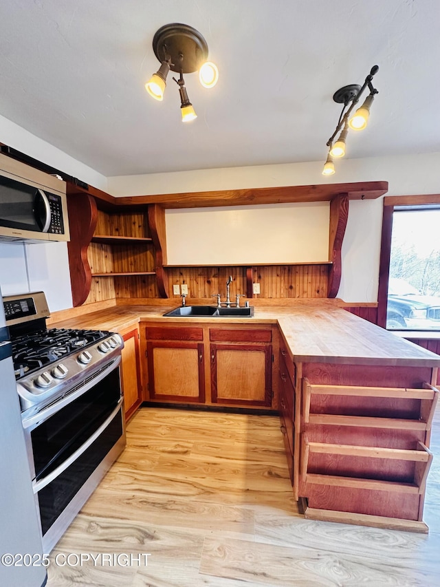 kitchen featuring a peninsula, stainless steel appliances, light wood-style floors, open shelves, and a sink