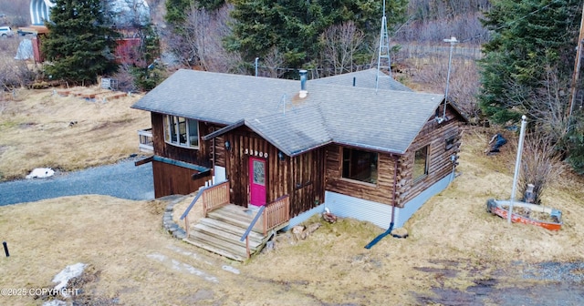 view of front of home with roof with shingles, log exterior, and dirt driveway