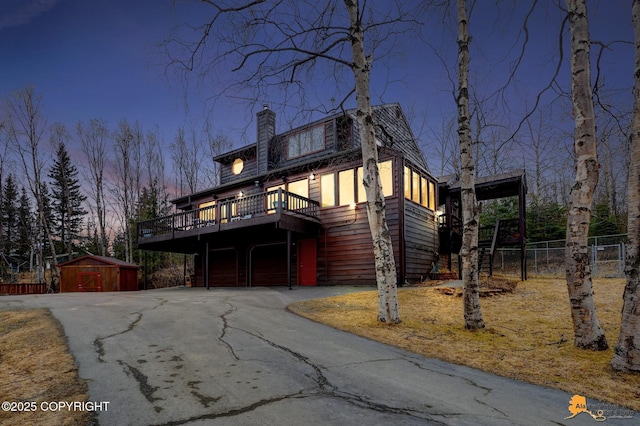 view of front of property with aphalt driveway, an outdoor structure, fence, a wooden deck, and a chimney