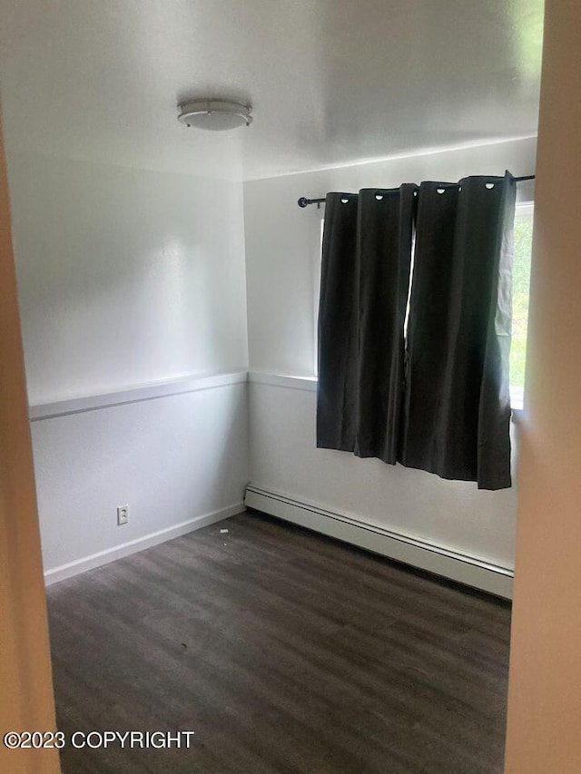 spare room featuring baseboard heating, wood finished floors, and baseboards