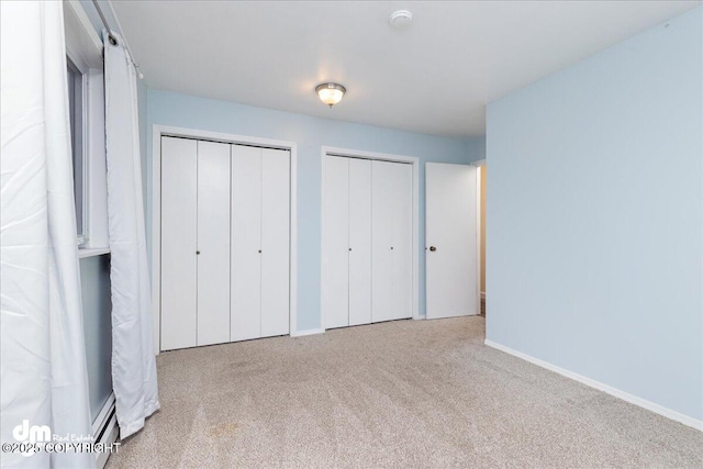 unfurnished bedroom with baseboard heating, baseboards, two closets, and carpet floors