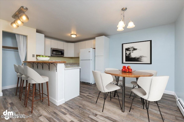 kitchen featuring a kitchen bar, stainless steel microwave, wood finished floors, freestanding refrigerator, and a peninsula