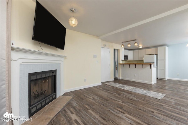 unfurnished living room featuring a tile fireplace, dark wood-type flooring, and baseboards