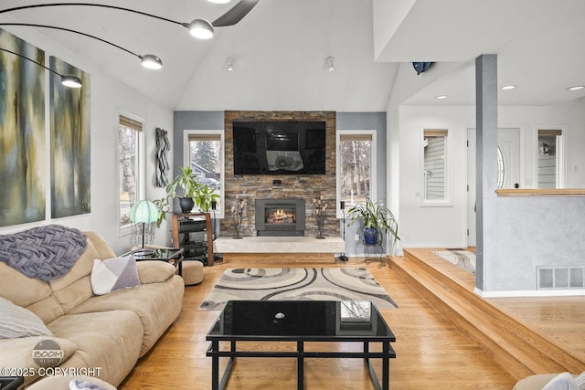 living room featuring visible vents, baseboards, lofted ceiling, a stone fireplace, and wood finished floors