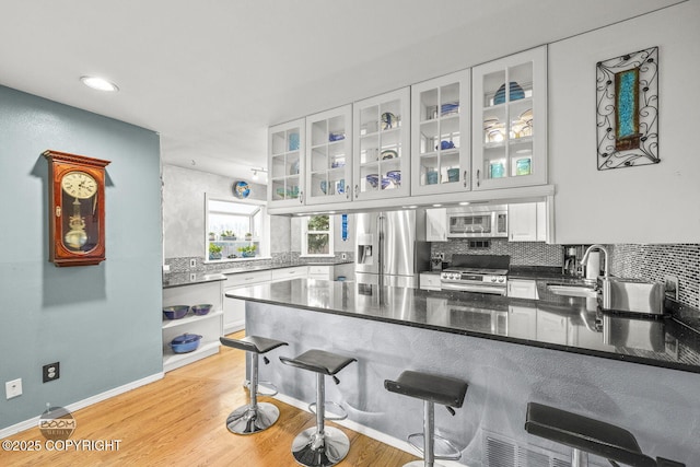 kitchen with a peninsula, a sink, decorative backsplash, light wood-style floors, and appliances with stainless steel finishes