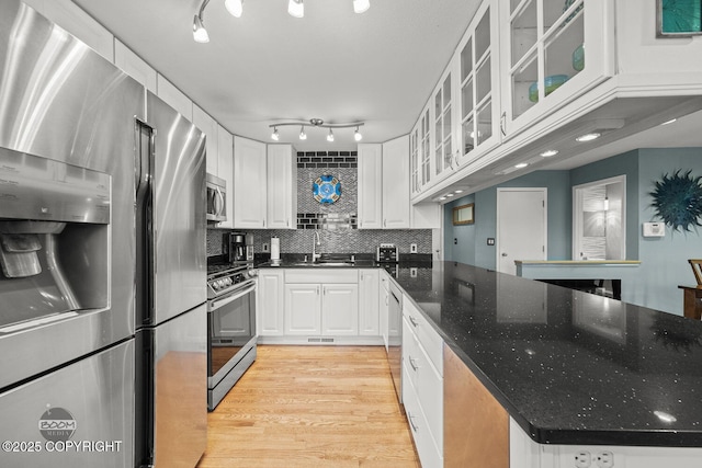 kitchen featuring backsplash, appliances with stainless steel finishes, light wood-style floors, white cabinetry, and a sink