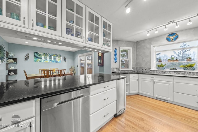 kitchen featuring dark stone countertops, white cabinetry, light wood-style flooring, glass insert cabinets, and stainless steel dishwasher