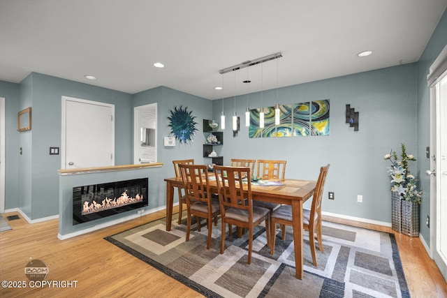 dining room with visible vents, baseboards, recessed lighting, wood finished floors, and a glass covered fireplace