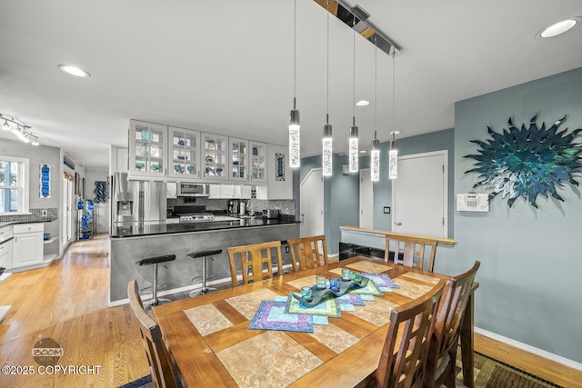 dining room featuring arched walkways, recessed lighting, light wood-type flooring, and baseboards