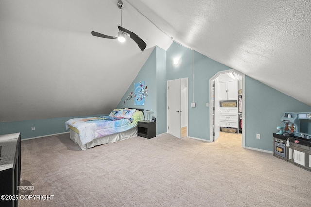 bedroom with a walk in closet, ceiling fan, vaulted ceiling, carpet flooring, and a textured ceiling