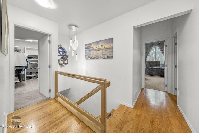 hall featuring an upstairs landing, light wood-style flooring, light colored carpet, and baseboards