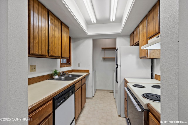 kitchen featuring under cabinet range hood, white appliances, a sink, light countertops, and light floors