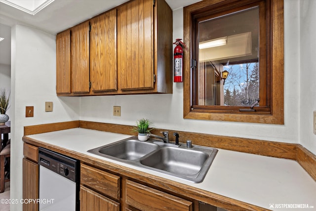 kitchen with light countertops, brown cabinets, white dishwasher, and a sink