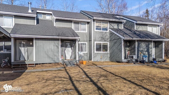 back of property with entry steps, a yard, and roof with shingles