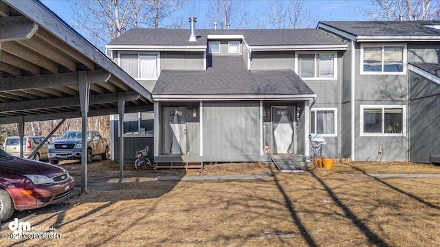 rear view of house featuring a carport, entry steps, and a shingled roof